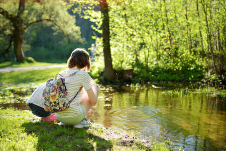 Two cute young sisters having fun by a river on warm spring day. Children playing together by a water. Outdoor family activities in early spring.の写真素材