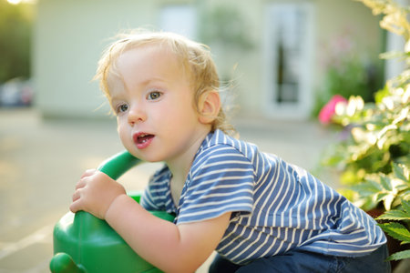 Cute toddler boy watering flowers in the garden at summer day. Child using watering can on sunny...