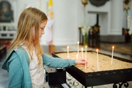 Cute little girl lighting a candle in a church. A child holding small candle in a chapel.の写真素材