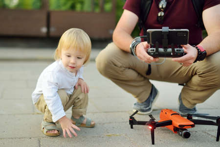 Father and son watching and navigating a drone. Cute toddler boy helping his father to operate a drone by remote control. Family leisure.の写真素材