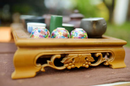 Tea pot and several cups on wooden table for traditional chinese tea ceremony outdoors.