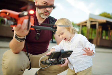 Father and son watching and navigating a drone. Cute toddler boy helping his father to operate a...
