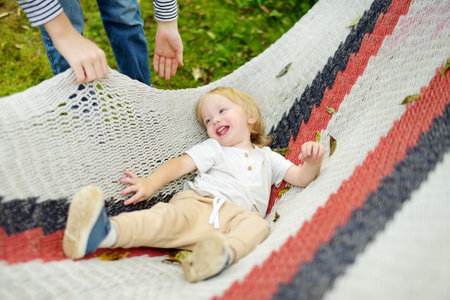 Happy toddler boy relaxing in hammock on beautiful summer day. Cute child having fun in summer park. Family leisure at summer.の写真素材