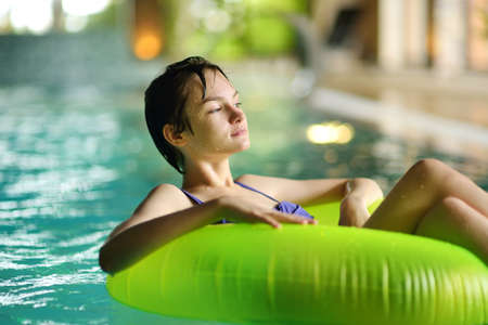 Cute young girl playing with inflatable ring in indoor pool. Child learning to swim. Kid having fun with water toys. Family fun in a pool. Activities for family with kids.の写真素材