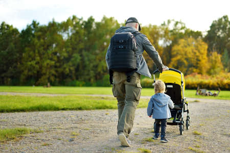 Young father walking in autumn park with toddler son in pushchair. Man pushing a stroller for toddler boy. Active family time at fall.の写真素材
