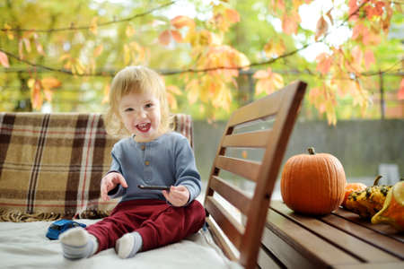 Funny toddler boy playing with variuos decorative pumpkins outdoors on sunny autumn day. Child exploring nature. Autumn activities for small kids.の写真素材