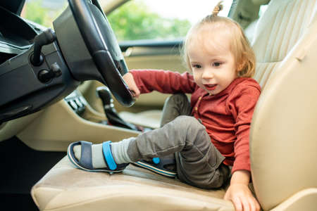 Adorable toddler boy playing in the driver's seat. Cute little son sitting in fathers car. Small...