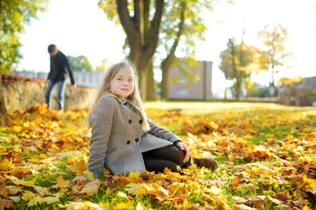 Adorable young girl having fun on beautiful autumn day. Happy child playing in autumn park. Kid gathering yellow fall foliage. Autumn activities for children.の写真素材