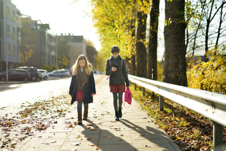 Cute young sisters with backpacks heading to school on cold autumn morningの写真素材