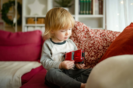 Cute toddler boy playing with red toy car. Small child having fun with toys. Kid spending time in a cozy living room at home. Family leisure indoors.の写真素材