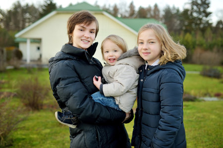 Two big sisters and their toddler brother having fun outdoors. Two young girls holding their sibling...