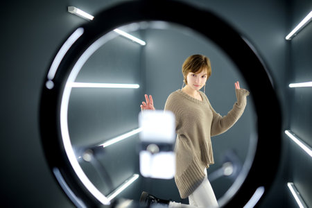 Beautiful teenage girl taking a selfie picture with mobile phone in light of the ring lamp. Trend,...