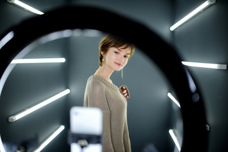 Beautiful teenage girl taking a selfie picture with mobile phone in light of the ring lamp. Trend,...
