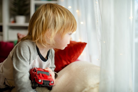 Cute toddler boy playing with red toy car. Small child having fun with toys. Kid spending time in a cozy living room at home. Family leisure indoors.の写真素材