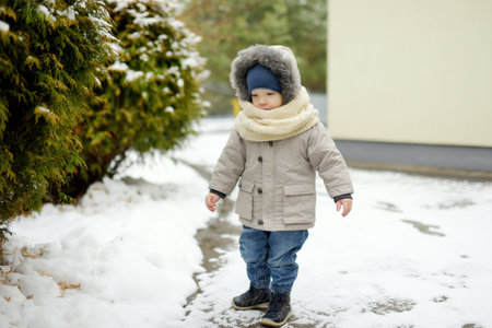 Adorable toddler boy having fun in a backyard on snowy winter day. Cute child wearing warm clothes playing in a snow. Winter activities for family with kids.の写真素材