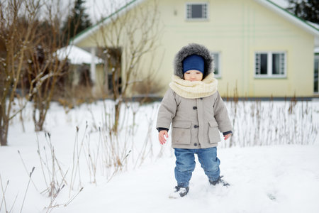 Adorable toddler boy having fun in a backyard on snowy winter day. Cute child wearing warm clothes playing in a snow. Winter activities for family with kids.の写真素材
