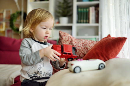 Cute toddler boy playing with red toy car. Small child having fun with toys. Kid spending time in a cozy living room at home. Family leisure indoors.の写真素材