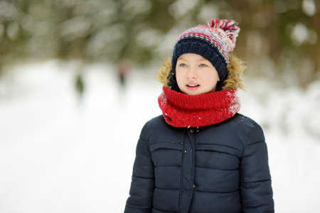 Cute young girl having fun on a walk in snow covered pine forest on chilly winter day. Child exploring nature. Winter activities for kids.の写真素材