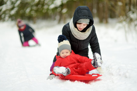 Cute young girl and her toddler brother having fun on a walk in snow covered pine forest on chilly winter day. Child exploring nature. Winter activities for kids.の写真素材