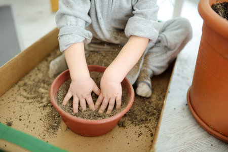 Cute toddler boy playing with a soil in flower pot. Small child having fun with natural materials....