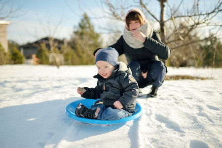 Funny toddler boy and his big teenage sister having fun outdoors on chilly winter day. Children...