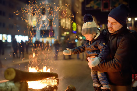 Father and son throwing a log into fire at the celebration of Restoration of the State Day in...