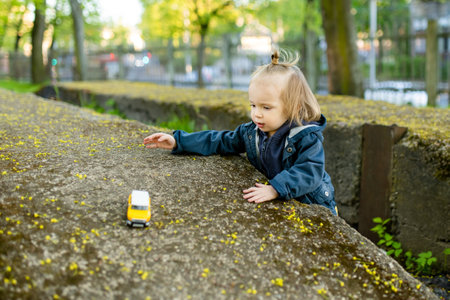 Cute toddler boy playing with yellow toy car outdoors. Small child having fun with toys.の写真素材