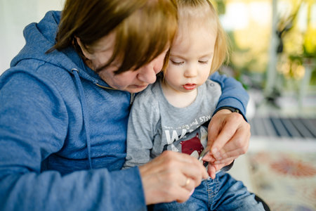 Grandmother cutting her toddler grandsons fingernails with small manicure scissors. Child sitting on...