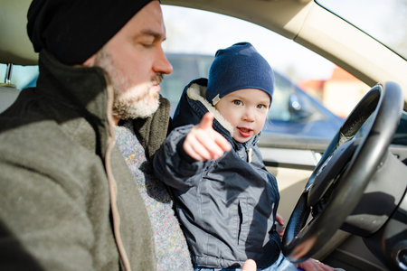 Adorable toddler boy playing in the driver's seat. Cute little son sitting in fathers car. Small...