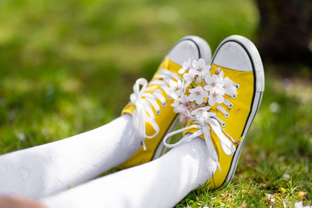 Female feet in bright yellow sneakers on green grass. Sitting in city park on sunny summer day. Outdoor leisure.の写真素材