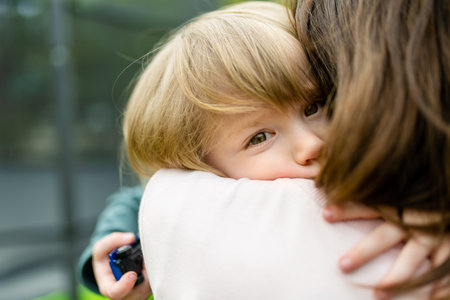 Cute funny toddler boy in his mothers arms. Mom and son having fun on sunny autumn day in a park. Adorable son being held by his mommy.の写真素材