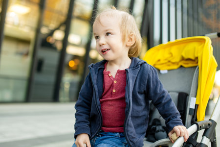 Sweet toddler boy sitting in a stroller outdoors. Little child in pram. Infant kid in pushchair. City walks with kids. Family leisure with little child.の写真素材