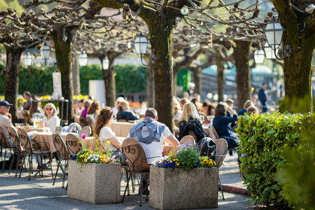 BELAGGIO, ITALY - APRIL 2022: Tourists and locals spending sunny spring day in Belaggio, a town on the shore of Lake Como. Charming location with typical Italian atmosphere. Belaggio, Lombardy, Italy.のeditorial素材