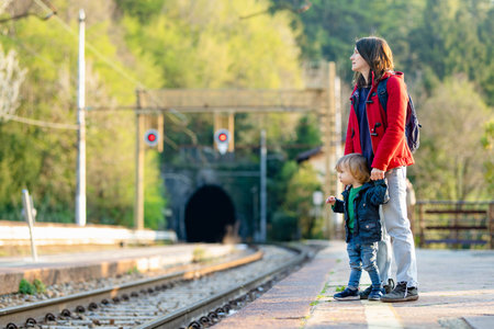 Young mother and her toddler son on a railway station. Mom and little child waiting for a train on a platform. Family ready to travel. Going on vacation with small kids.の写真素材