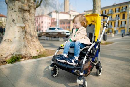 Sweet toddler boy sitting in a stroller in Lecco town. Little child in pram. City walks with kids....