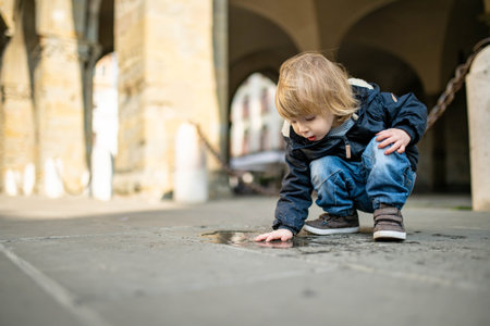 Cute toddler boy playing in a puddle on the street of Bergamo. Little child having fun exploring in Citta Alta, upper district of Bergamo. Bergamo, Lombardy, Italy.の写真素材