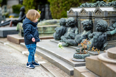 Little toddler boy visiting Cimitero Monumentale di Milano or Monumental Cemetery of Milan, one of the two largest cemeteries in Milan, noted for the abundance of artistic tombs and monuments.の写真素材