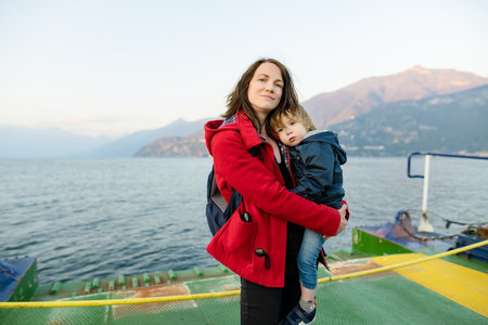 Young mother and her toddler son on a ferry. Mom and little child traveling by ferry on Como Lake in Italy. Going on vacation with small kids.の写真素材