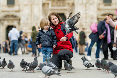 Young mother and her toddler son feeding the pigeons on the Cathedral Square or Piazza del Duomo in the center of Milan, Lombardy, Italy.の写真素材