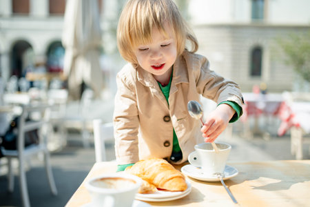 Cute toddler boy having hot chocolate in outdoor cafe. Small child drinking hot beverage on sunny terrace in Lecco. Spending good time on vacation with kids on Lake Como. Lecco, Lombardy, Italy.の写真素材