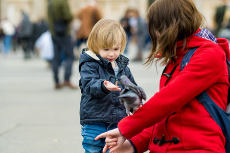 Young mother and her toddler son feeding the pigeons on the Cathedral Square or Piazza del Duomo in the center of Milan, Lombardy, Italy.の写真素材