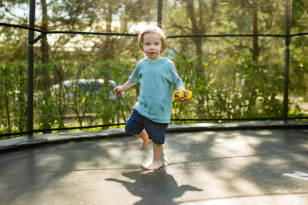 Cute toddler boy jumping on a trampoline in a backyard on warm and sunny summer day. Sports and exercises for children. Summer outdoor leisure activities.の写真素材