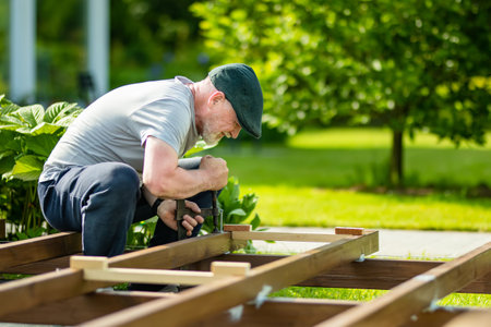 Senior man working on a project in his garden. Man constructing a wooden terrace on his backyard.の写真素材