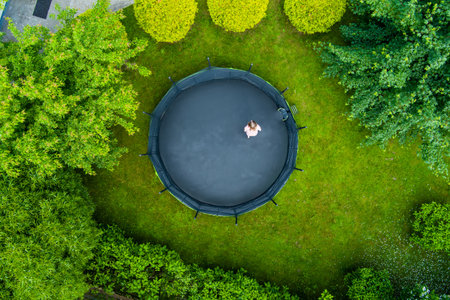 Aerial top-down view of a teenage girl jumping on a trampoline in a backyard. Backyard kids fun. Summer outdoor leisure activities.の写真素材