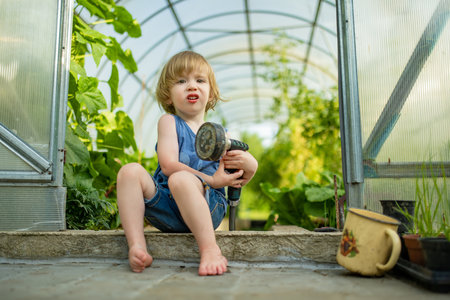 Cute toddler boy having fun in a greenhouse on sunny summer day. Child helping with daily chores. Gardening activity for kids.の写真素材