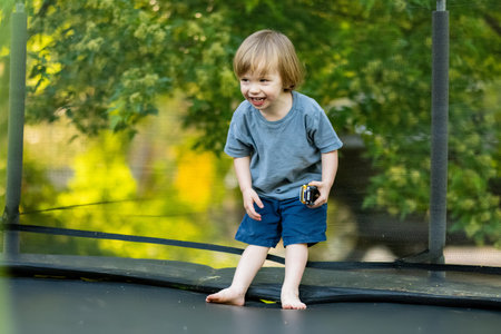 Cute toddler boy jumping on a trampoline in a backyard on warm and sunny summer day. Sports and exercises for children. Summer outdoor leisure activities.の写真素材