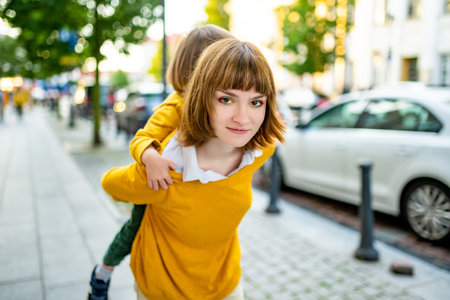 Cute big sister cuddling with her toddler brother. Adorable preteen girl piggybacking her small sibling. Children with large age gap. Siblings getting along.の写真素材