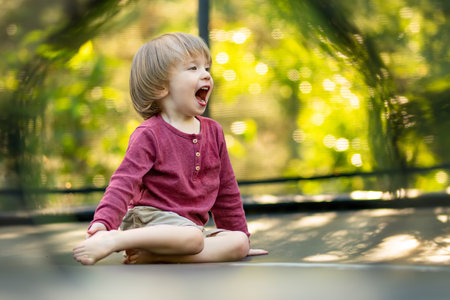 Cute toddler boy jumping on a trampoline in a backyard on warm and sunny summer day. Sports and exercises for children. Summer outdoor leisure activities.の写真素材