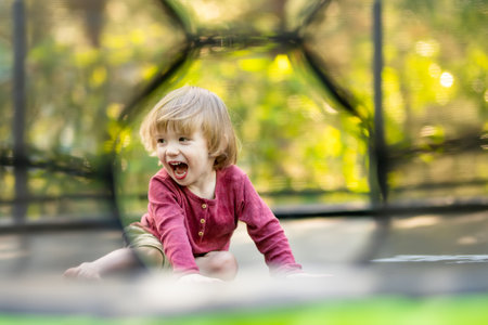 Cute toddler boy jumping on a trampoline in a backyard on warm and sunny summer day. Sports and exercises for children. Summer outdoor leisure activities.の写真素材