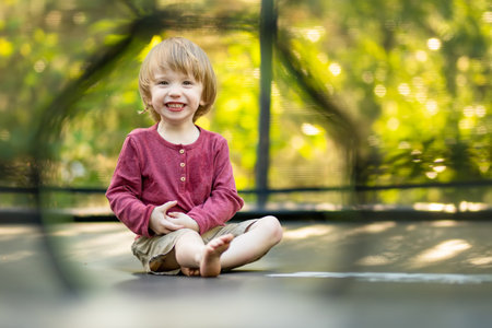 Cute toddler boy jumping on a trampoline in a backyard on warm and sunny summer day. Sports and exercises for children. Summer outdoor leisure activities.の写真素材